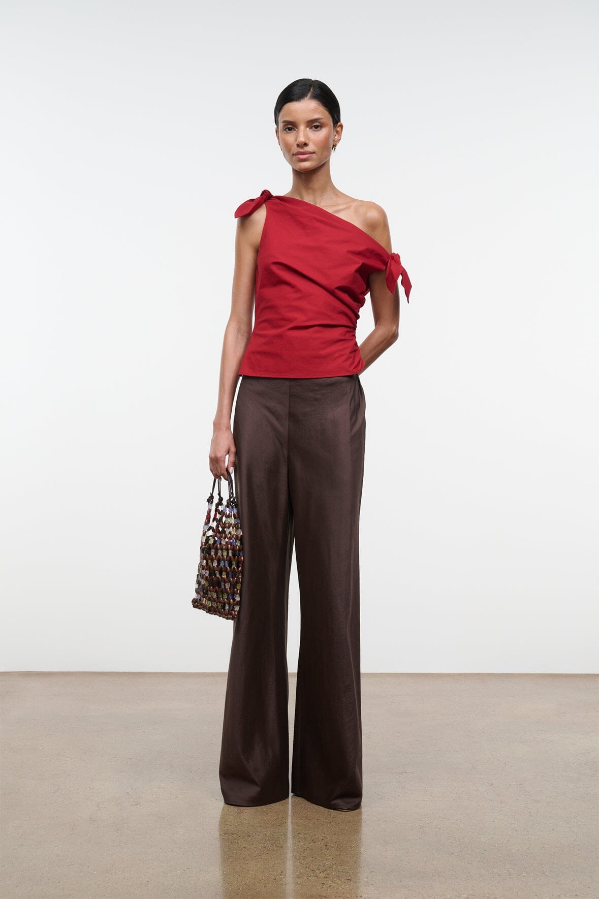Red asymmetrical one-shoulder draped top with knot and bow ties on one side.