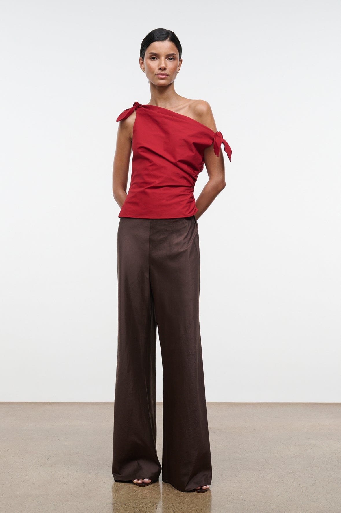 Red asymmetrical one-shoulder draped top with shoulder bow ties and side gathers.