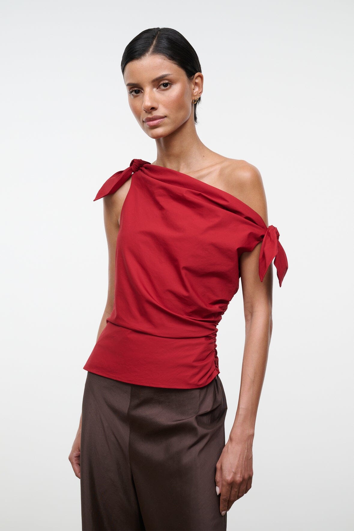 Red asymmetrical one-shoulder draped top with tied bow detail and side ruching.