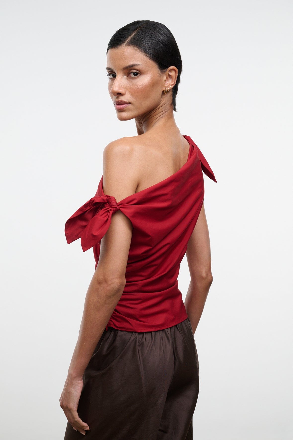 Side view of red asymmetrical one-shoulder draped top with shoulder bow ties.