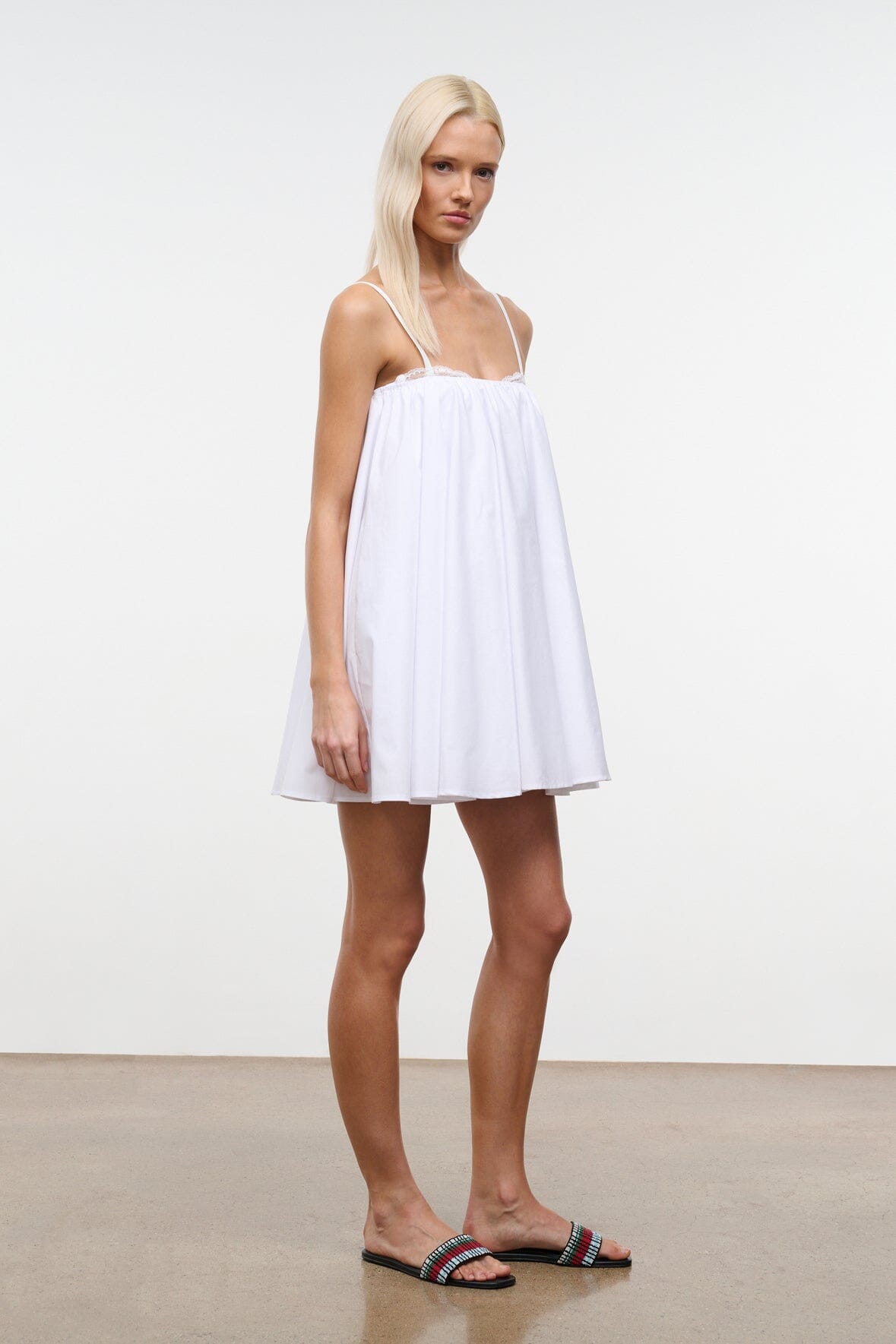 White mini babydoll dress with spaghetti straps, lace trim, and flared skirt.