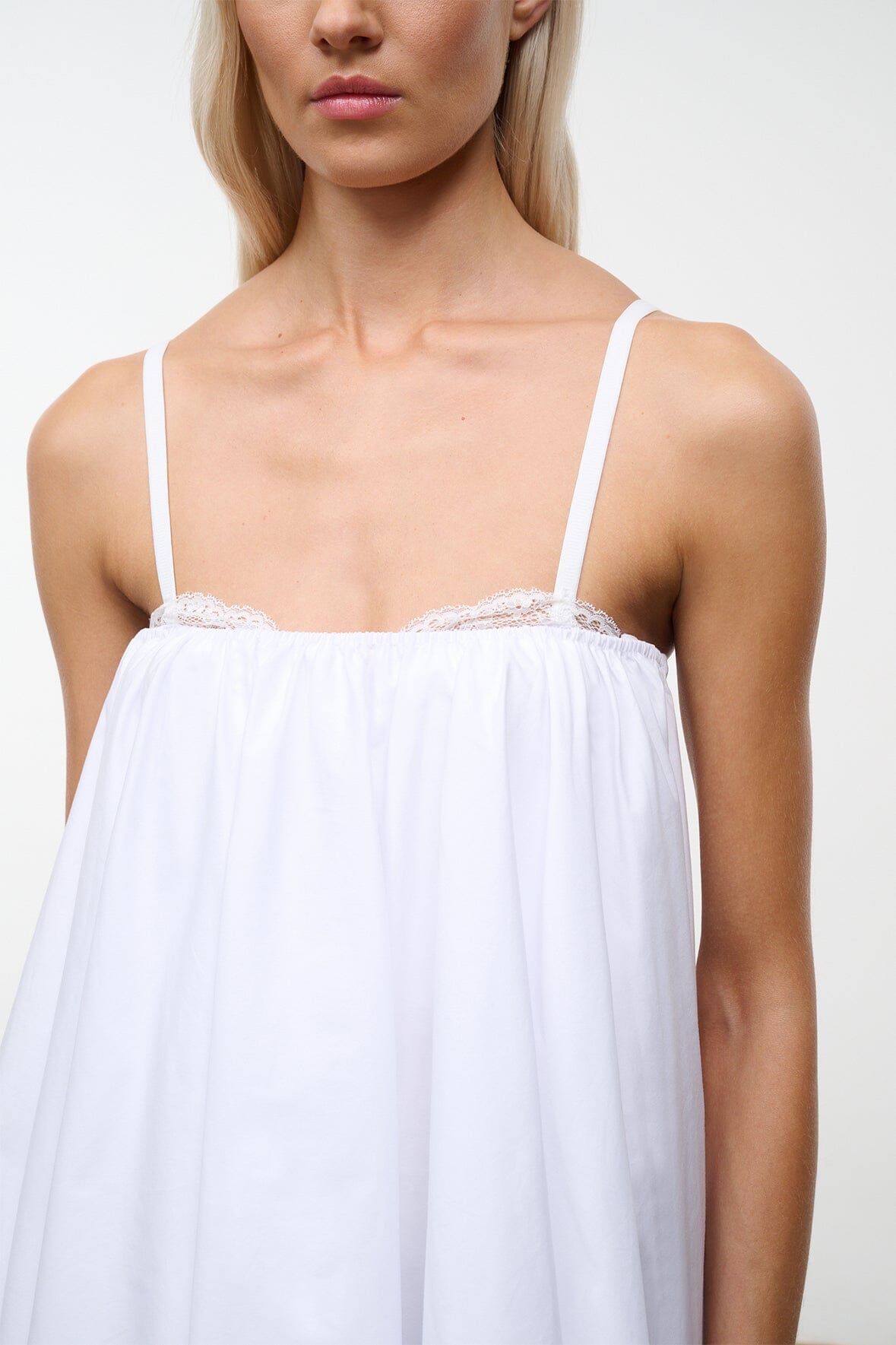 White mini dress bodice close-up with lace trim and thin spaghetti straps.