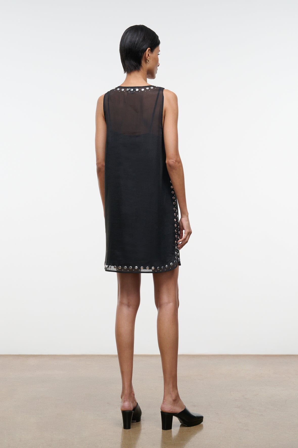 Black sleeveless mini dress, back view, with stud-trim hem and side accents