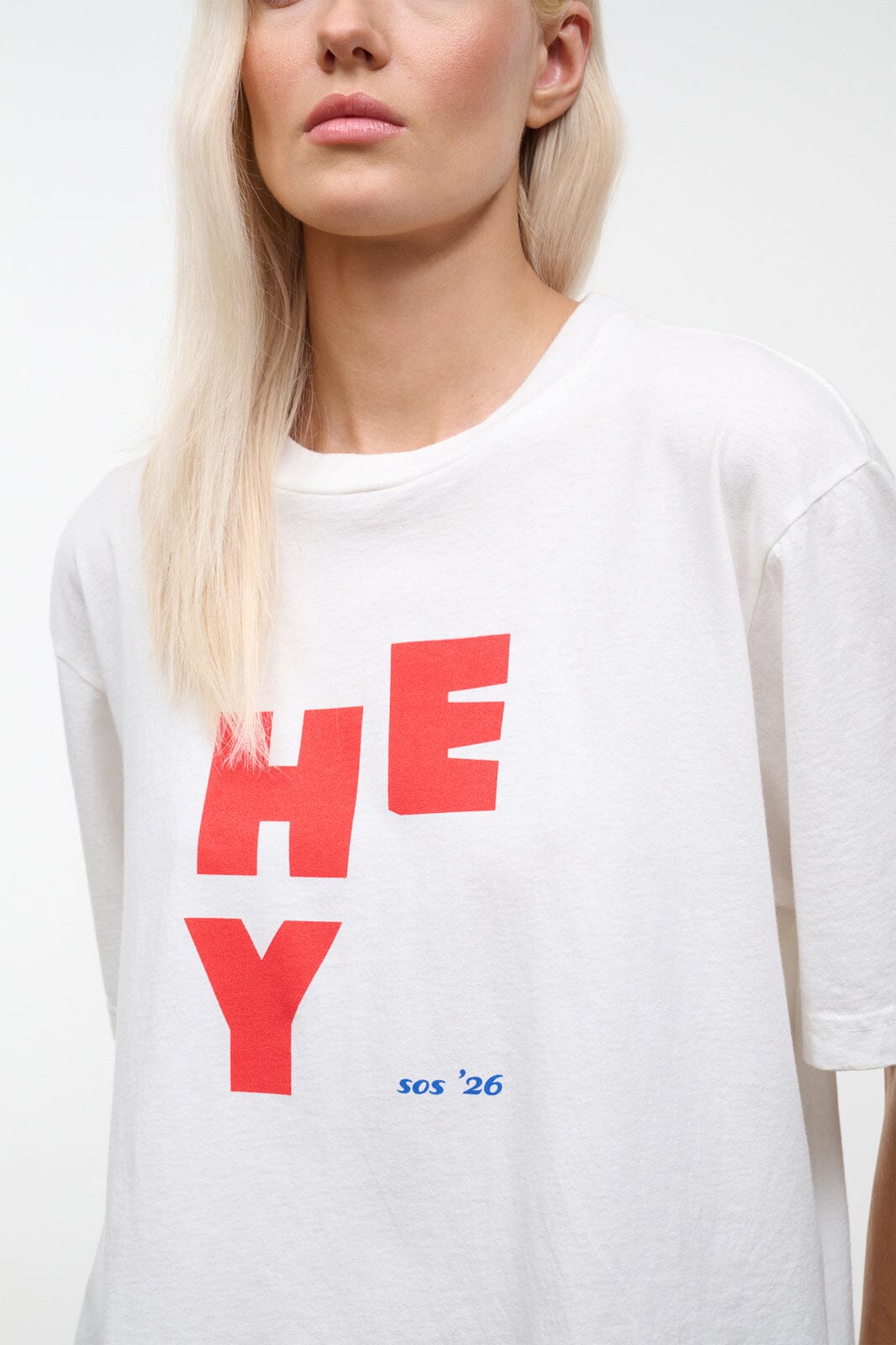 Close-up of white relaxed tee showing red “HEY” graphic and small blue “so’s ’26” text.