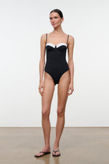 Black one-piece swimsuit with white bust panel and thin straps, standing full-body view