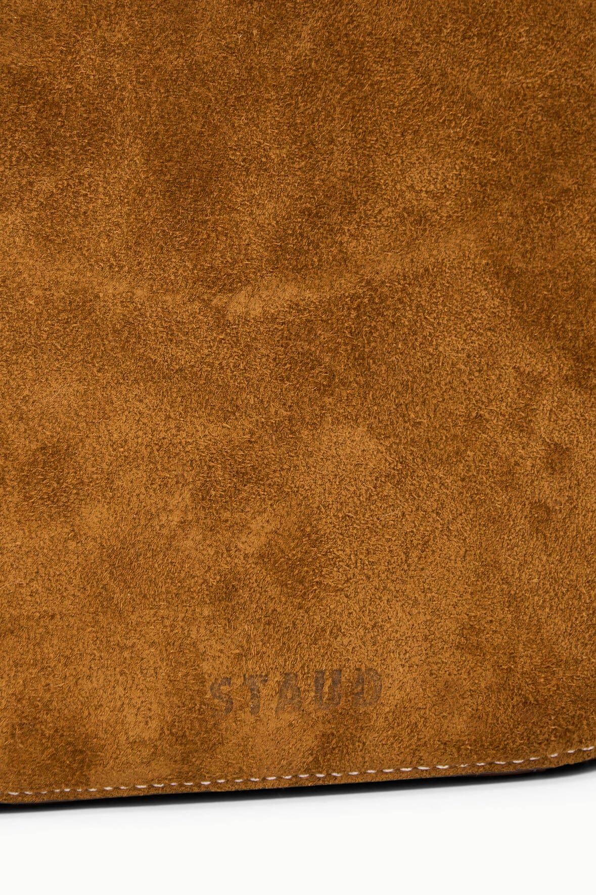 Tan suede saddle bag close-up of textured fabric and stitched bottom edge.
