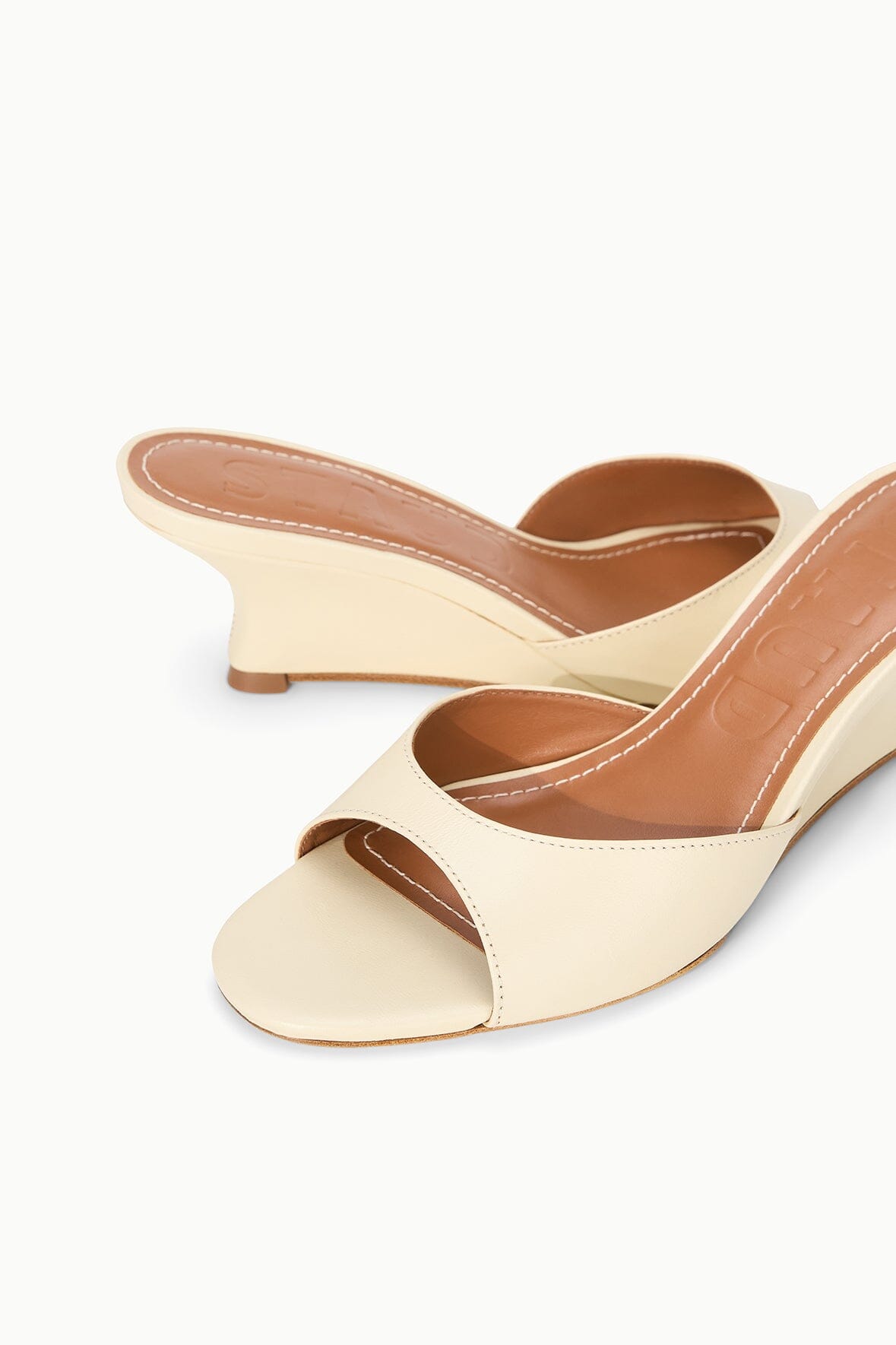Cream wedge slide sandals with tan interior and peep-toe opening