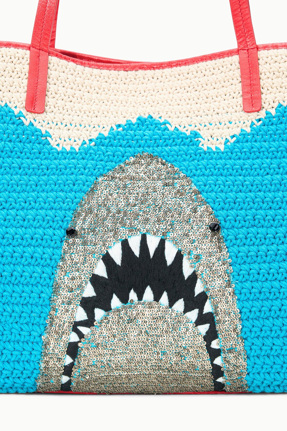 Front of blue crocheted tote bag with shark graphic and cream zigzag trim, red handles