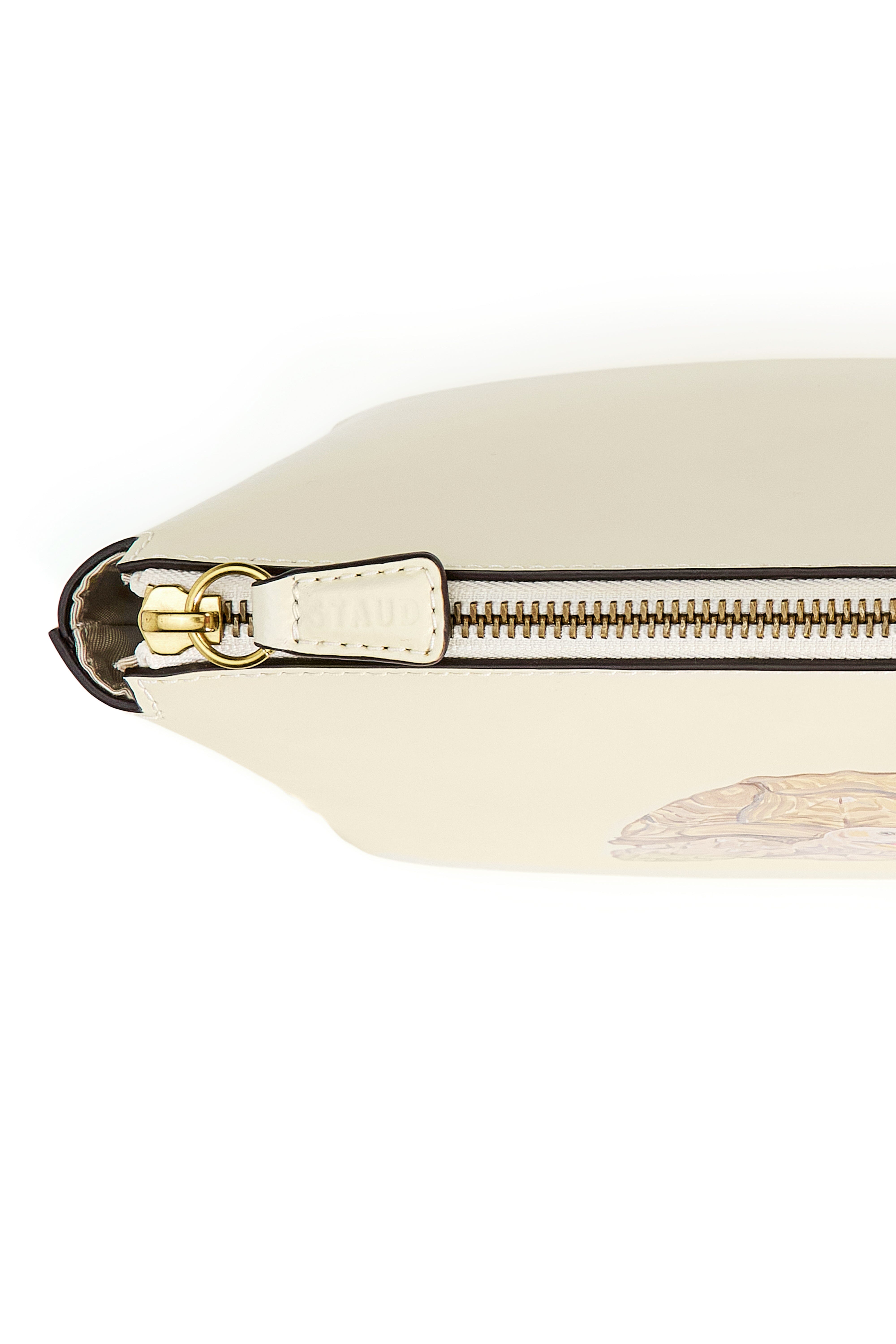Cream pouch detail with gold-tone zipper, leather tab, and strap