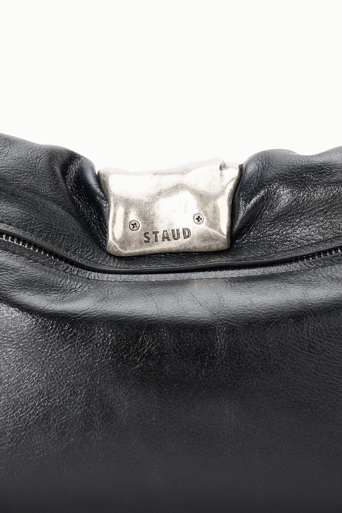 Black leather cuff clutch bag close-up of silver clasp plate with STAUD logo