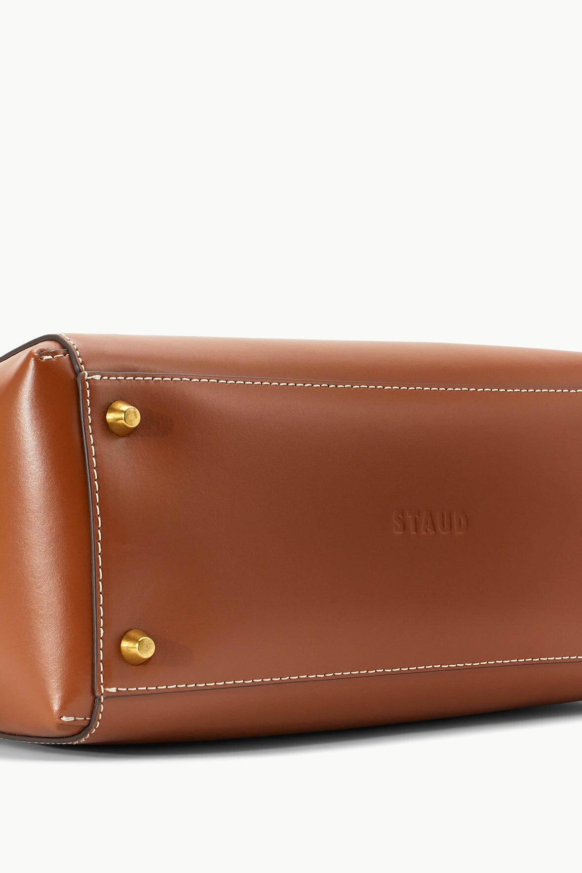 Tan leather bag front close-up with gold snaps and STAUD logo