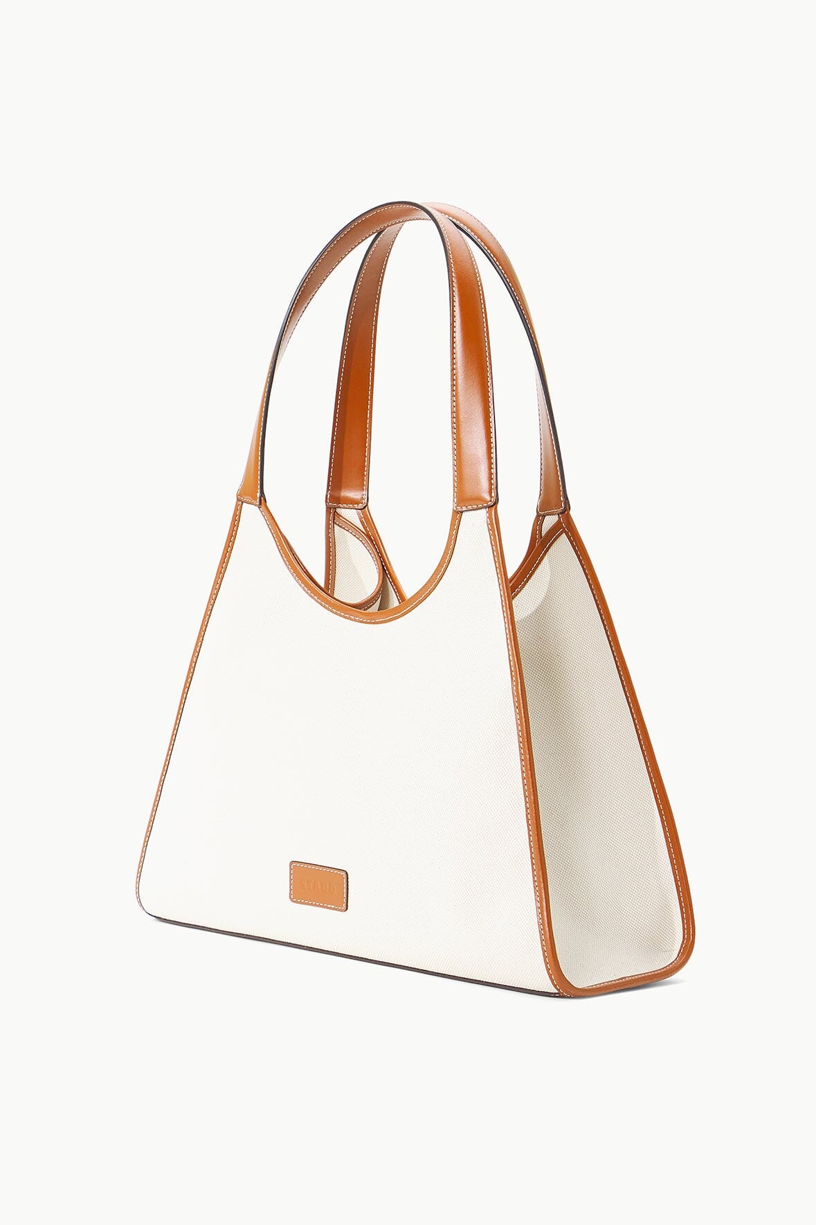 Cream canvas tote bag with tan leather handles and small tan logo plaque