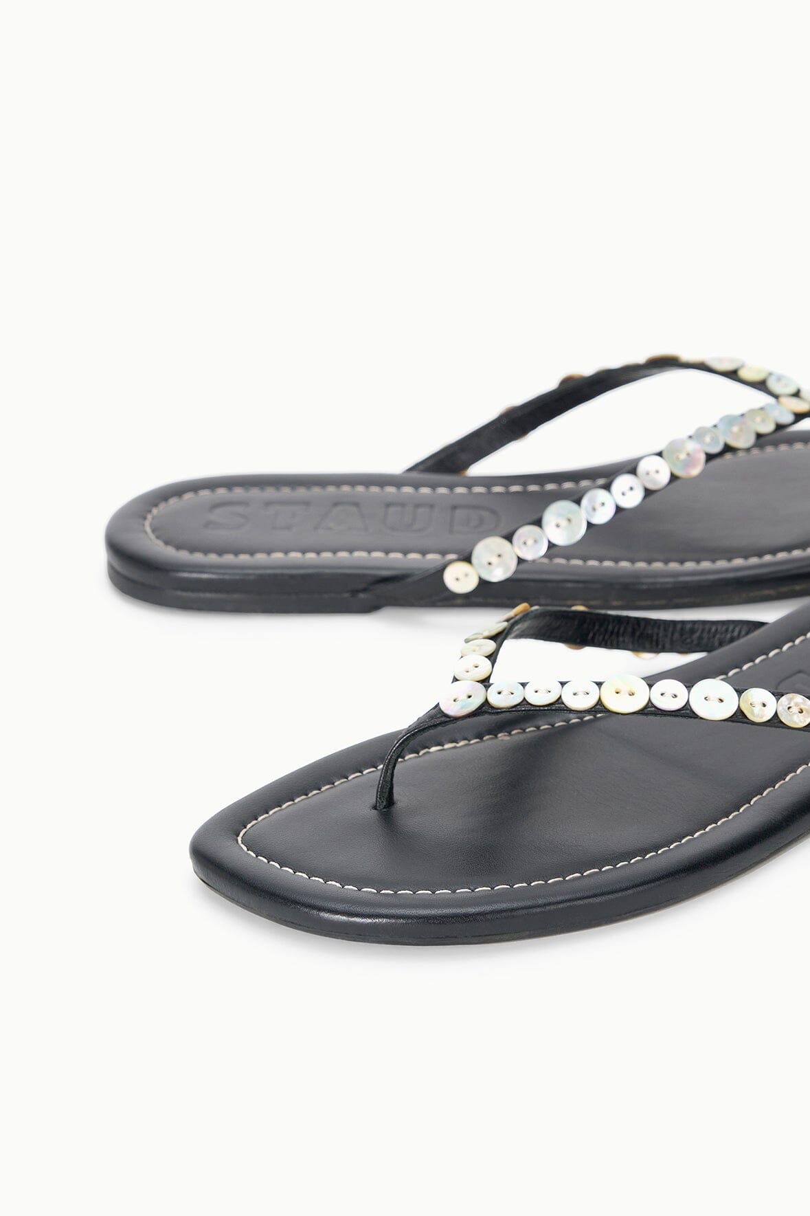 Black thong sandals close-up with pearl bead chain strap and stitching.