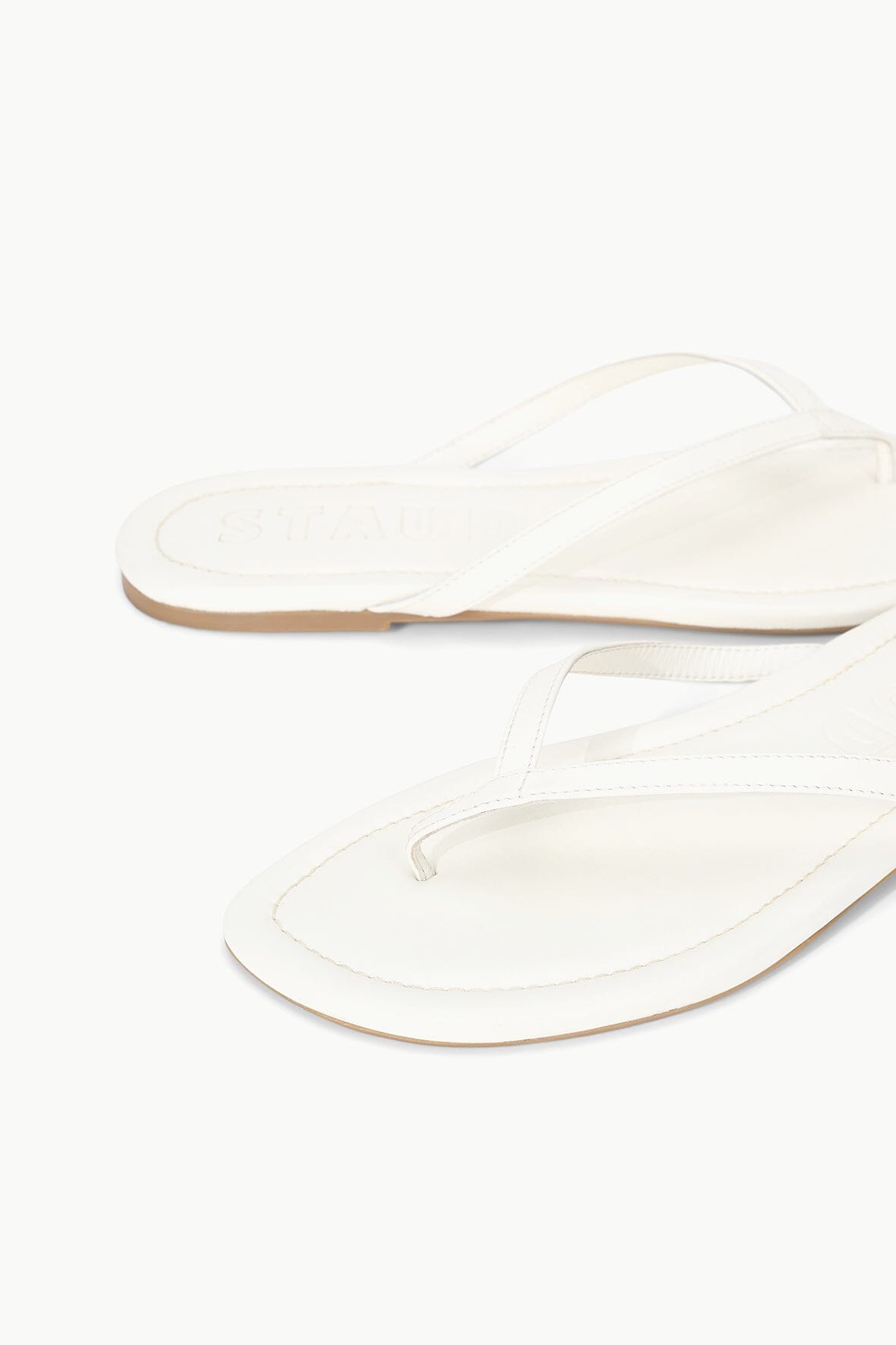 White thong sandals with front toe strap and flat sole, side view