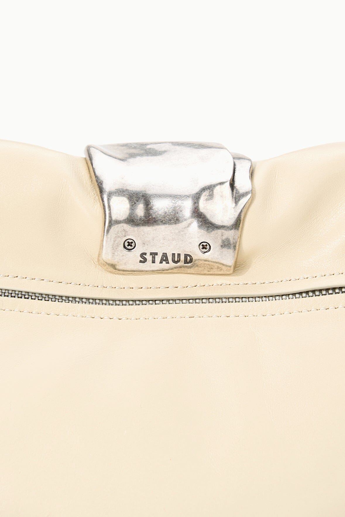 Silver clasp labeled STAUD on cream cuff clutch front panel.