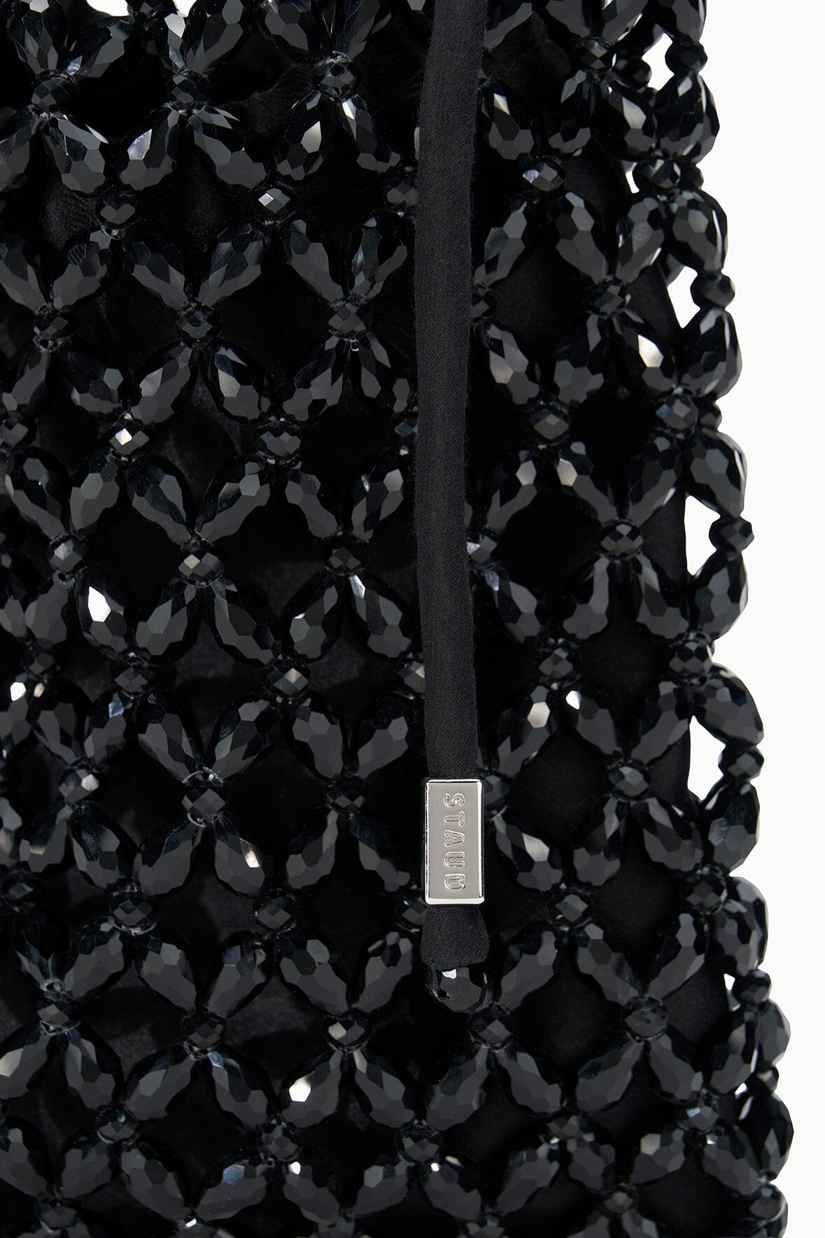Black beaded tote bag close-up with metal logo charm on woven mesh