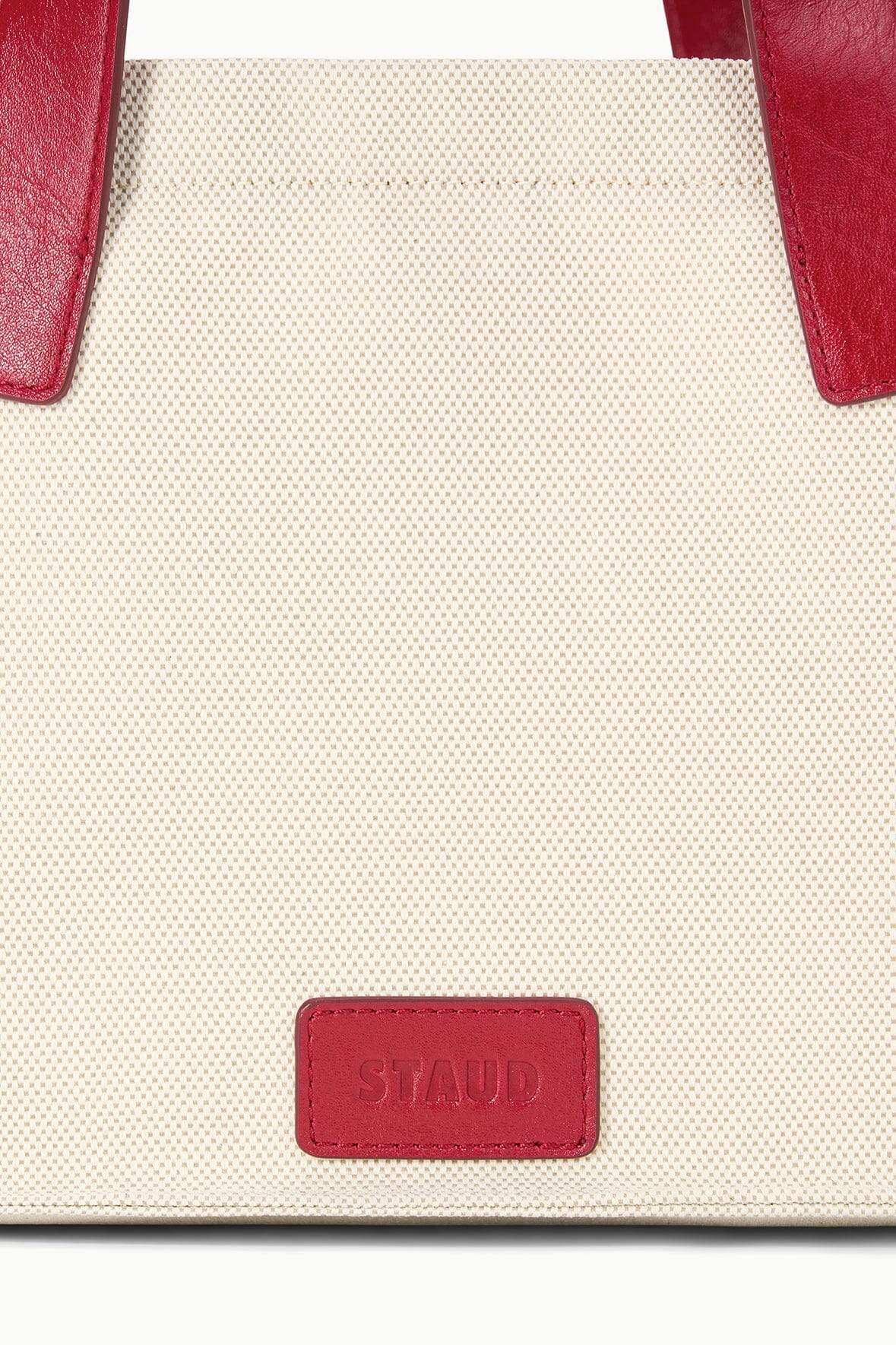 Cream tote bag front panel with red leather-look side tabs and red label patch