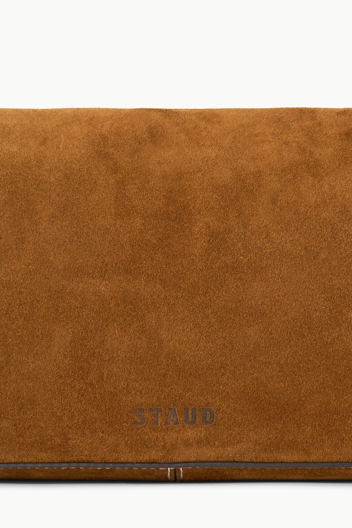 Tan suede bag flap close-up with stitched edge and STAUD logo