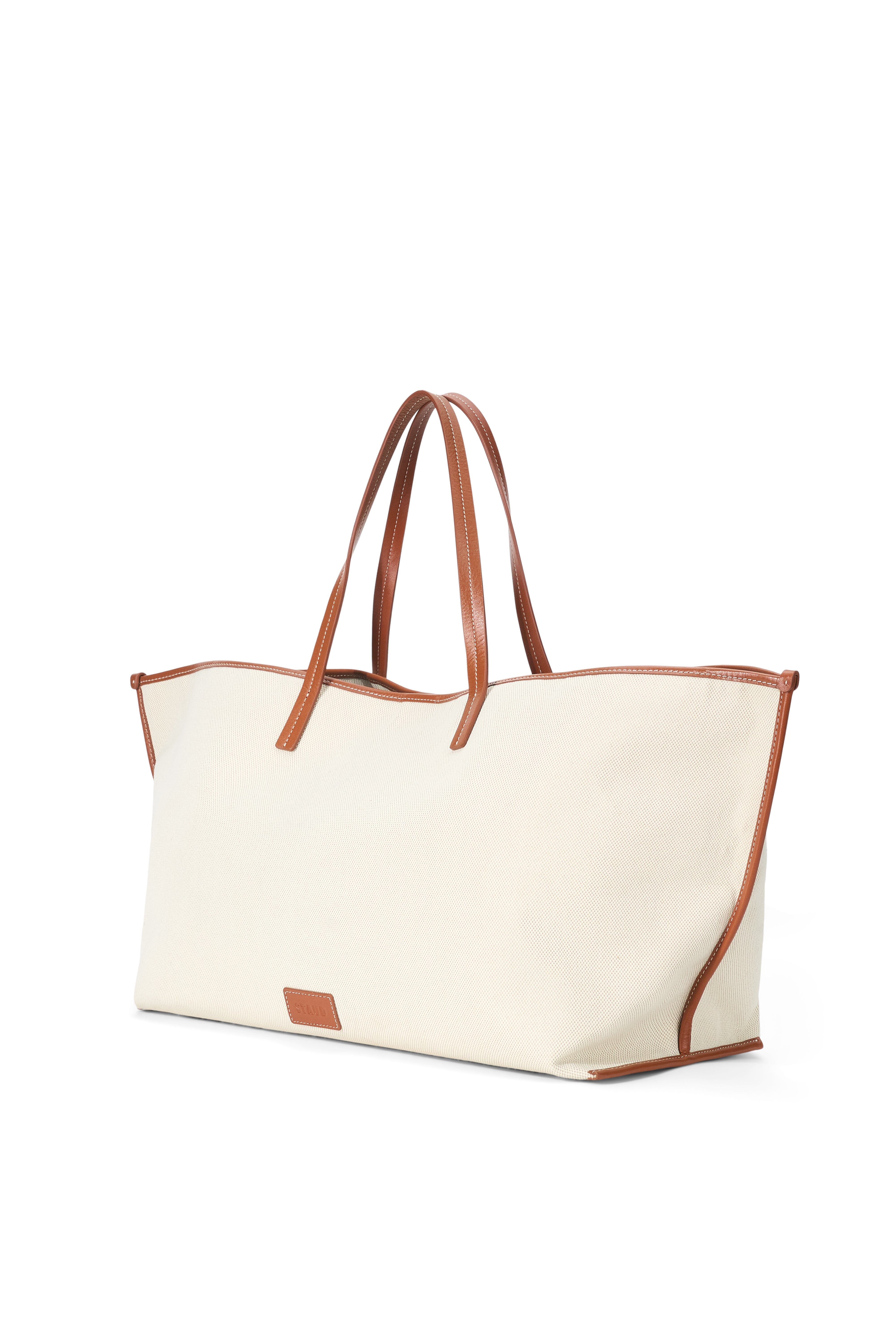 Cream canvas tote bag with tan leather handles and small leather corner patch