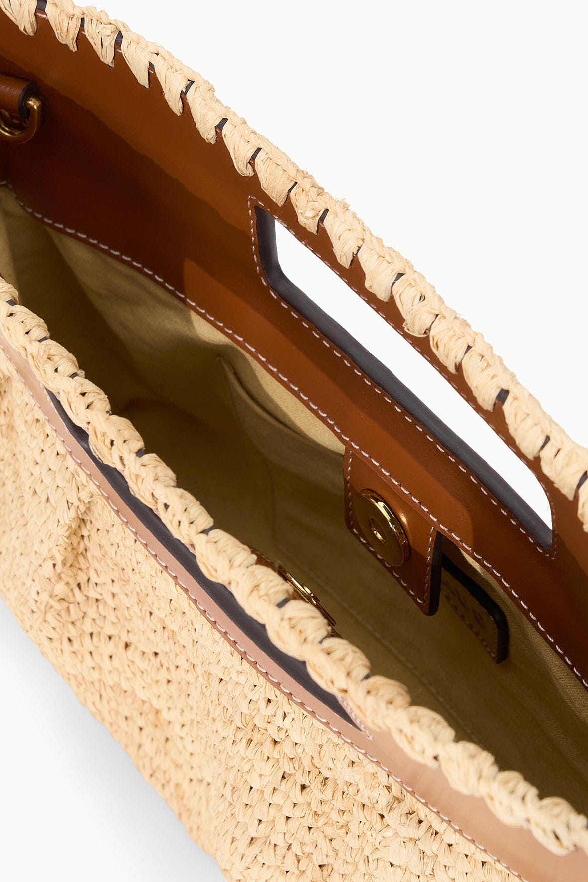 Open natural tan straw clutch showing brown lining and braided top edge.