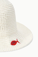 Close-up of off-white crochet bucket hat brim with red fish applique and brown leather patch.