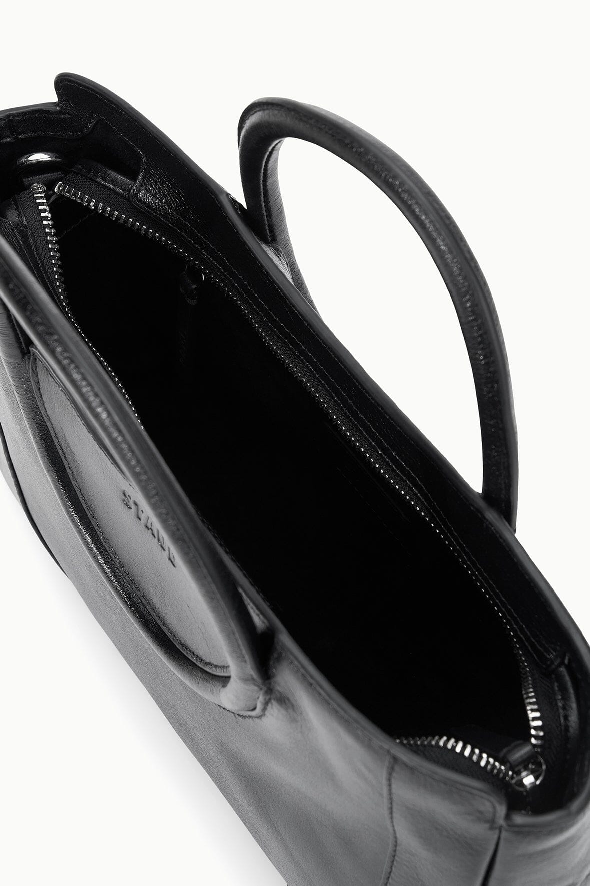Black mini satchel bag open view showing dark interior and stitched top edge