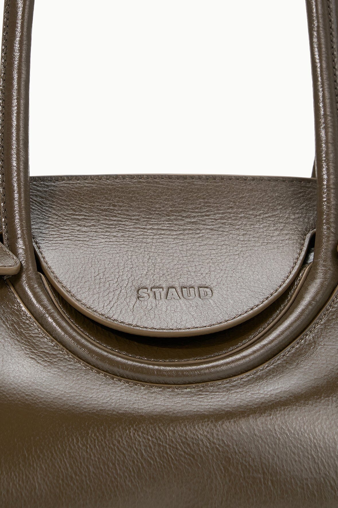 Brown leather shoulder bag close-up with embossed “STAUD” logo on front panel