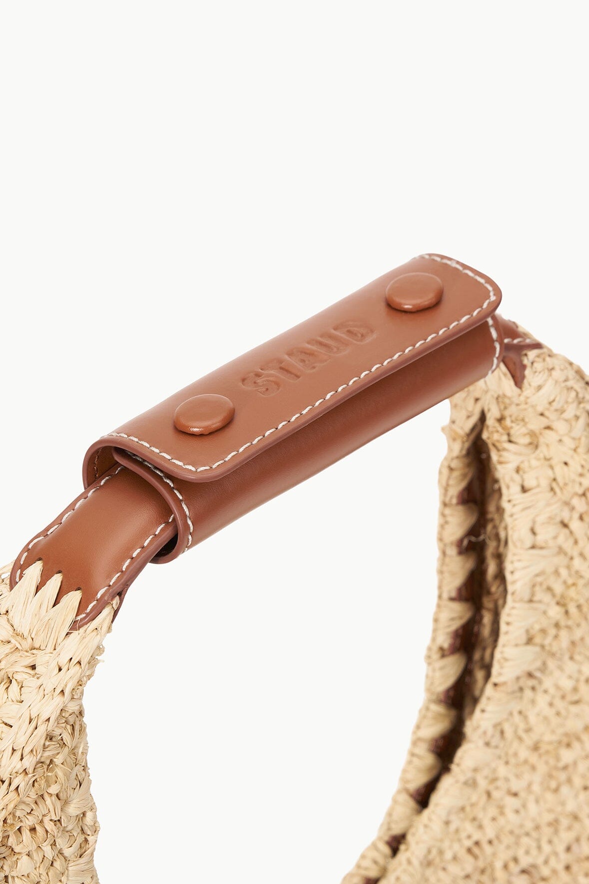 Brown leather strap with two snap buttons and stitched edge on raffia bag