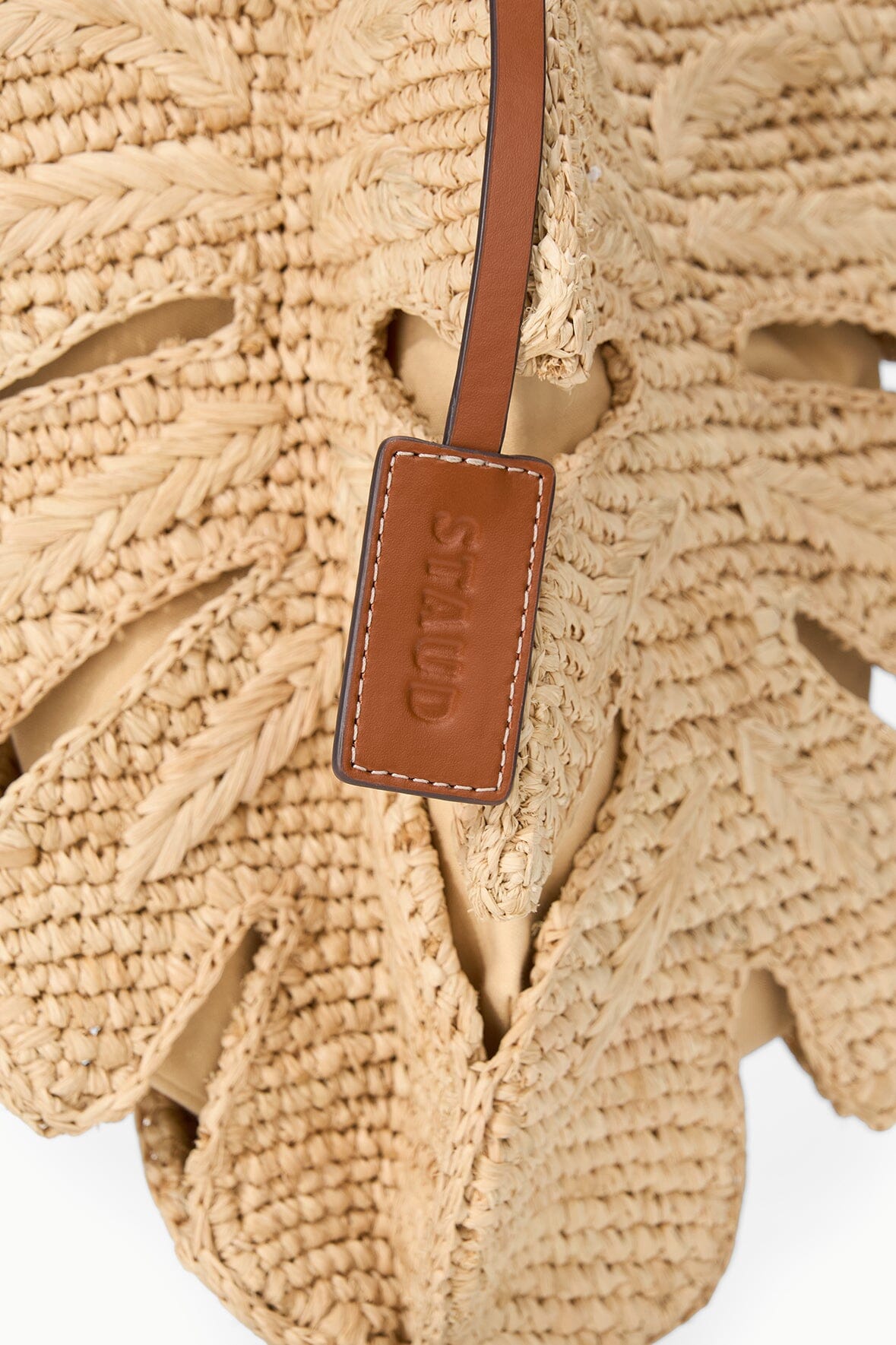 Close-up of tan leather tag on natural raffia leaf mini bag with stitched strap