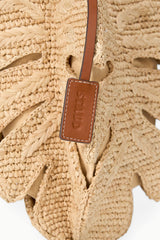 Close-up of tan leather tag on natural raffia leaf mini bag with stitched strap