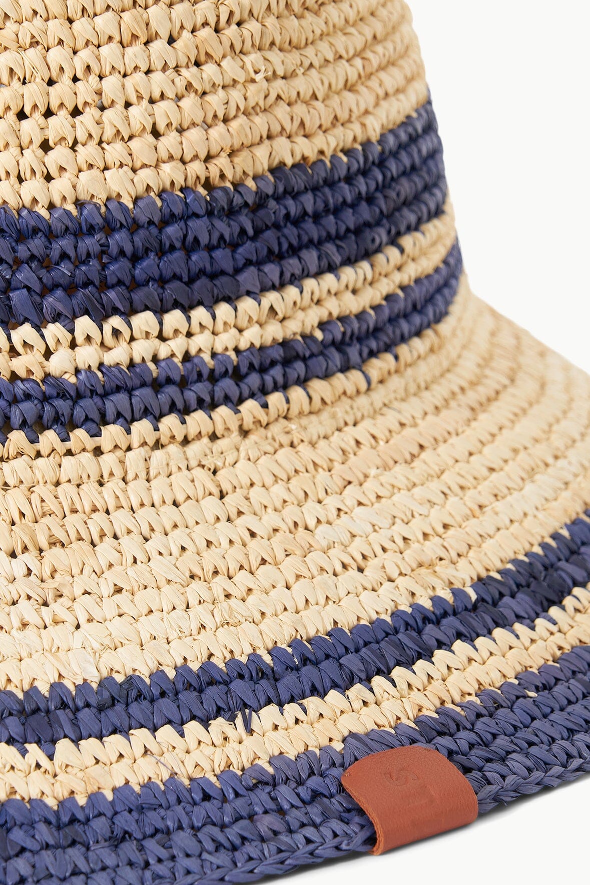 Striped straw bucket hat with navy bands and tan leather accent patch