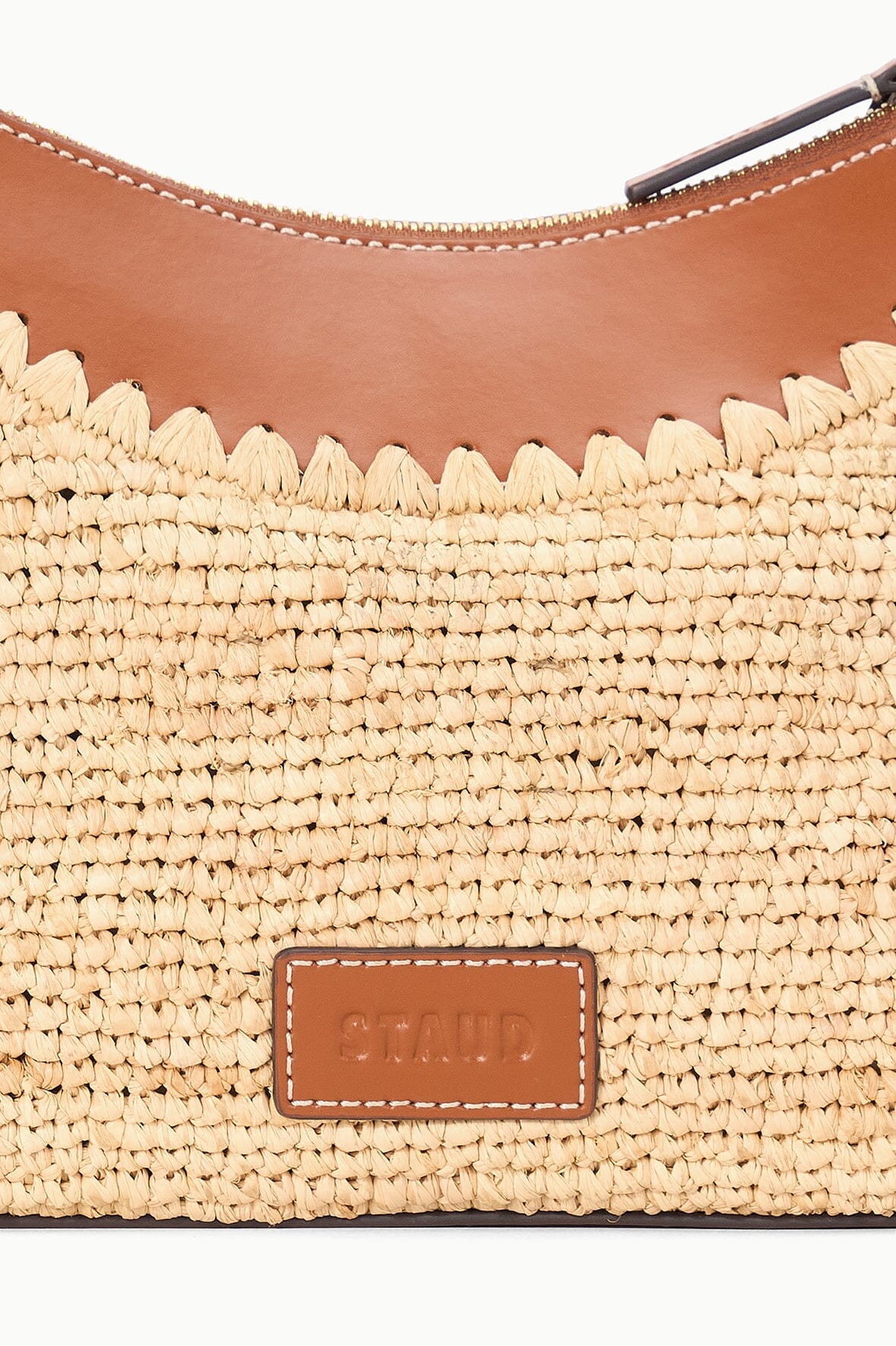 Natural tan raffia bag front with brown leather logo patch and scalloped trim