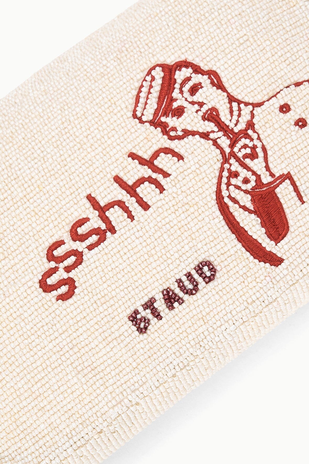 Close-up of cream tweed bag with red “ssshh” embroidery and decorative figure