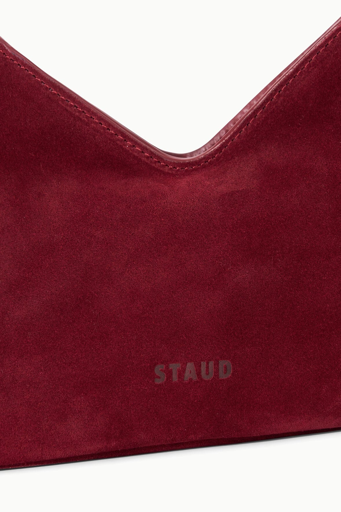 Burgundy suede shoulder bag close-up with logo and curved top opening