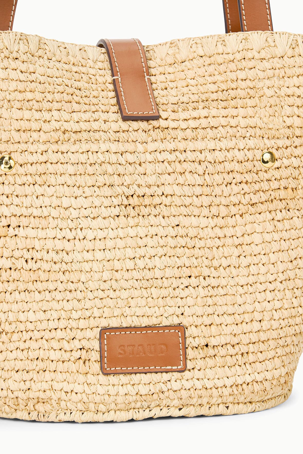 Natural tan woven tote bag close-up with tan leather label and gold-toned rivets