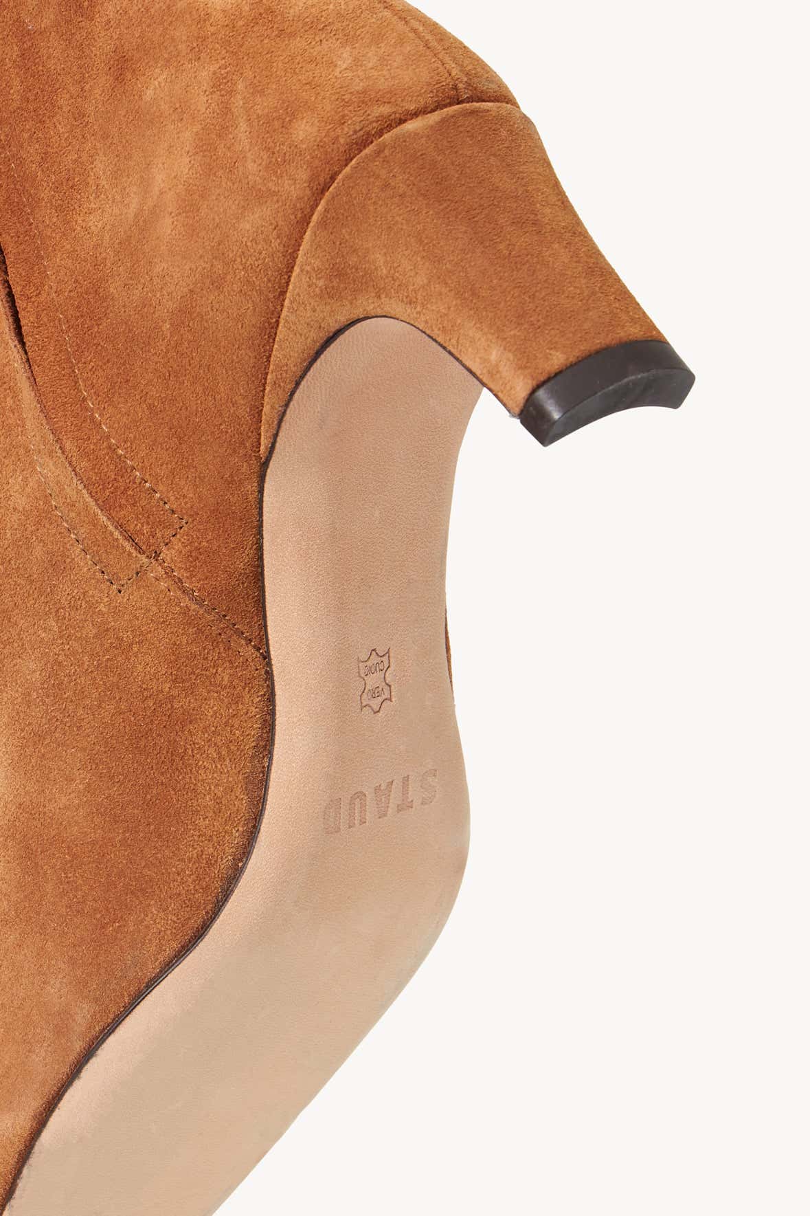 Close-up of tan suede ankle boot with logo patch and side zipper