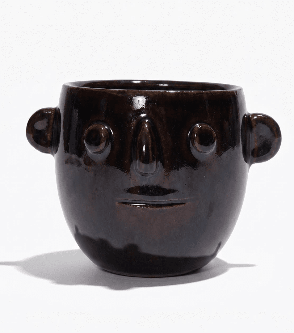 Ceramic candle pot with dark glossy finish and carved smiling face; side handles