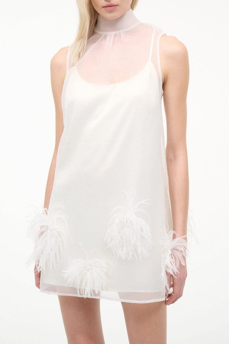 White mini dress with high neck, sleeveless sheer bodice, feather trim at hem