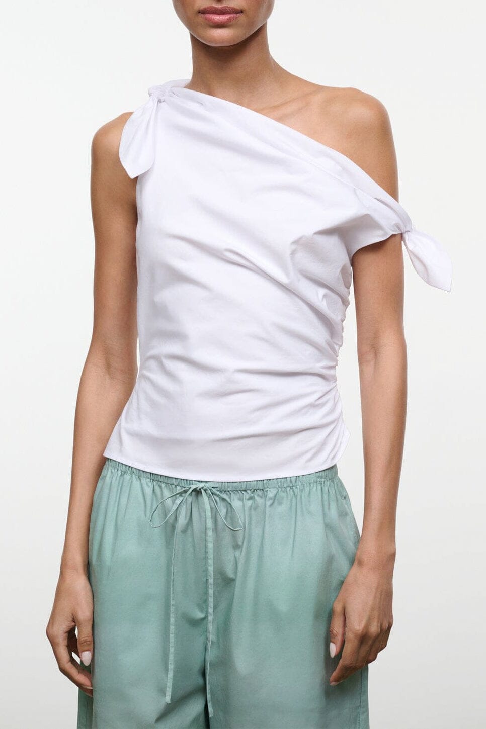 White one-shoulder wrap top with draped fabric and tied bow shoulder