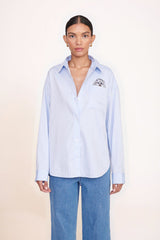 Light blue oversized button-up shirt with pointed collar and chest logo patch detail