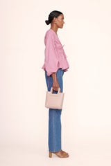 Blush leather mini tote bag worn by model, side view with top handle