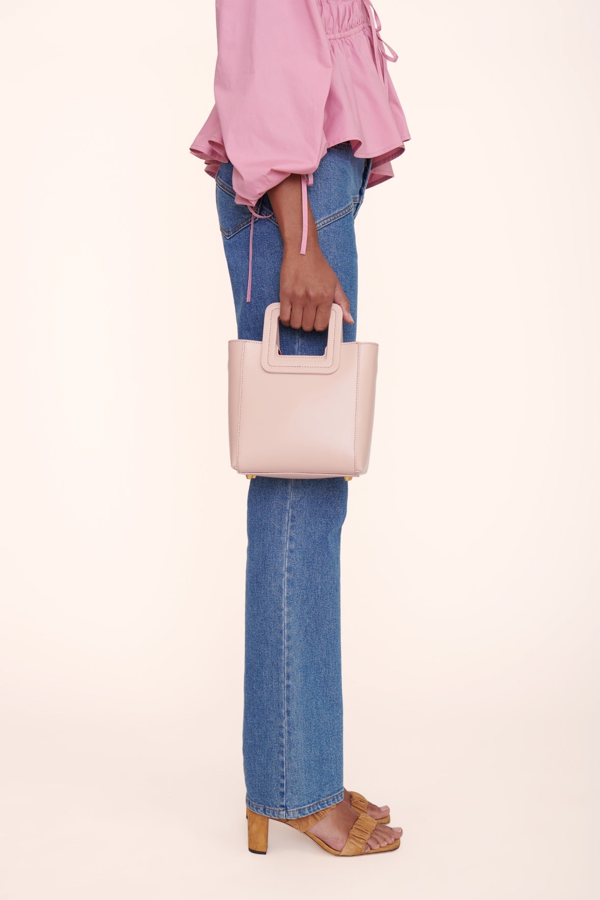 Blush leather mini tote bag held by model with top handle and open compartment